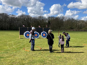 Two young visitors and an adult are coached by archers in Bowmen of Darenteford uniform at the farm open day.