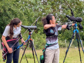 An archer checks the scope while another is ready to shoot