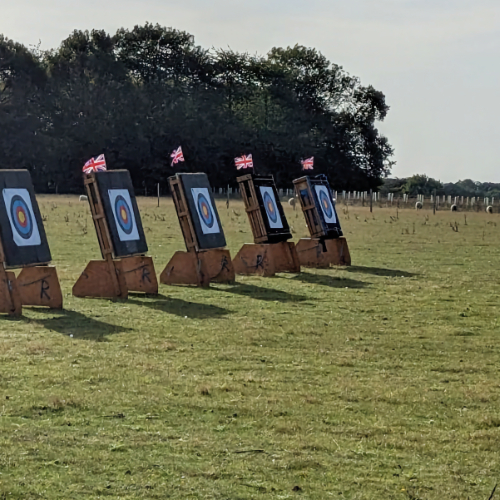 Five bosses are lined up on the field, topped with union flags to indicate movement of wind. In the background there is a field with a few grazing sheep.