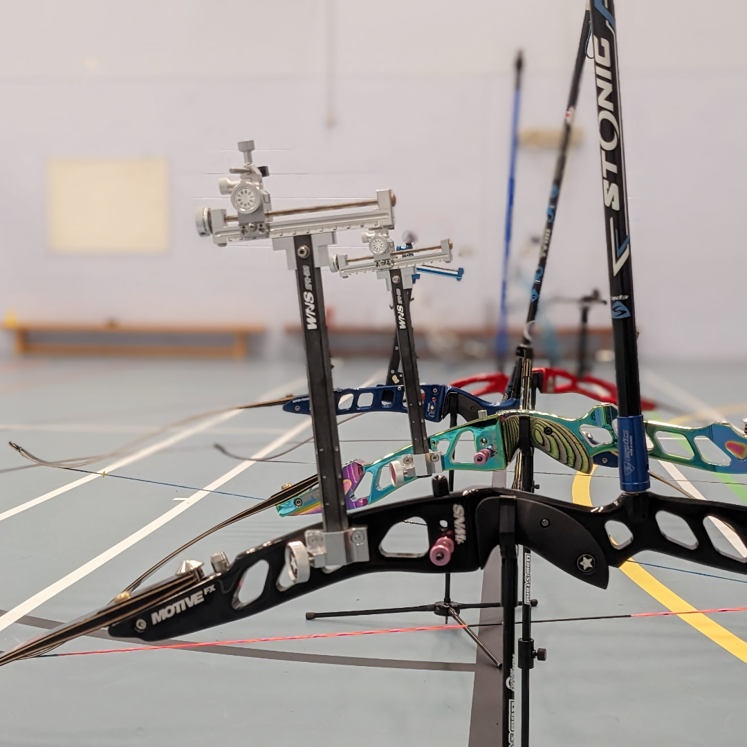 Four bows are on stands, they're pictured at eye level and are set up with sights and long rods. The closest bow has a Stonic branded longrod.